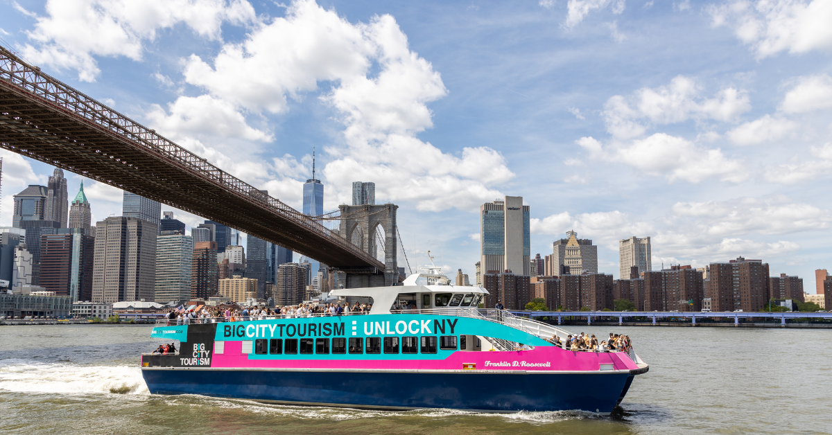 big-city-tourism-new-york-landmarks the Brooklyn bridge and Manhattan skyline including the one world trade center in the background of a freedom liberty cruise boat